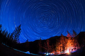 Star Trail in sky above the mountains fire in the tent camp