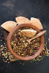 Clay plate with mexican bean soup served with pita bread, top view on a dark brown stone background