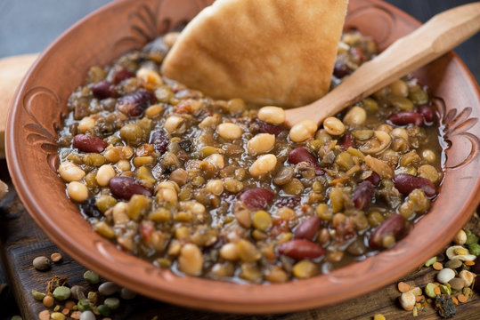 Close-up of a clay plate with thick soup cooked with variety of beans, selective focus