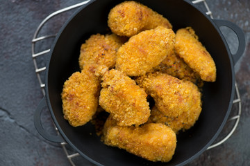 Cast-iron pan with fried breaded chicken wings, view from above, horizontal shot