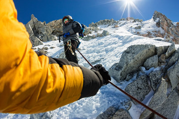 Tied climbers climbing mountain with snow field tied with a rope with ice axes and helmets first...