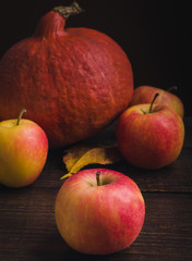 Pumpkin with apples and autumn leaves at wooden background.