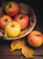 apples in the basket and autumn leaves at wooden background.