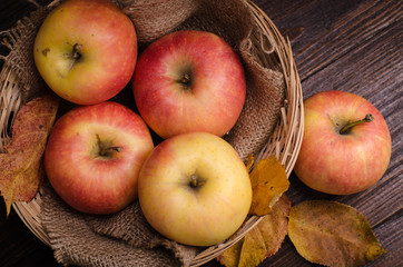 apples in the basket and autumn leaves on a wooden table.