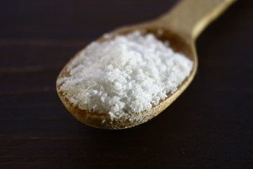 Fototapeta na wymiar White salt in a wooden spoon lies against a wooden background