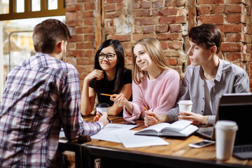 Young successful people are using a laptop, drinking coffee, talking and smiling while working in cafe