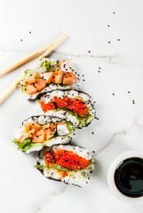Trend hybrid food. Japanese Asian cuisine. Mini sushi-tacos, sandwiches with salmon, hayashi wakame, daikon, ginger, red caviar. White marble table, with chopsticks, soy sauce. Copy space top view