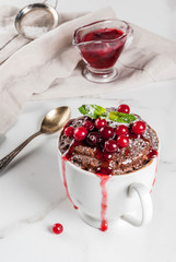 Winter, fall healthy breakfast or snack. The idea of a quick treat for Christmas. Chocolate mug cupkake in ceramic cup, with cranberry and sauce, powdered sugar. White marble table, copy space