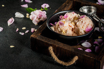 Summer refreshing desserts. Vegan diet food. Ice cream with rose petals and slices of almonds, on wooden old tray, on black stone table. With spoon for ice cream and ingredients. Copy space