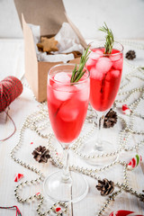 New Year's, Christmas drinks. Red alcohol cocktail with cranberry, liqueur, rosemary, with ice. On a white table, with Christmas candies, ornaments and pine cones. Copy space