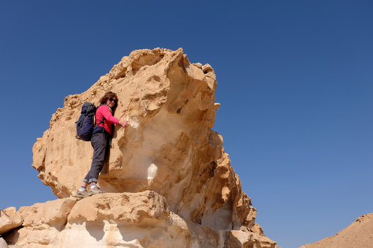 Middle aged female hiker climbing on yellow rock formation in Negev desert mountains.