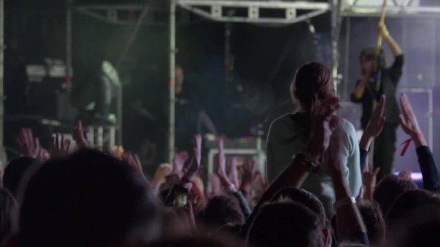 Handheld shot of many young people taking photographs with touch smart phone during a music entertainment public concert.Audience with hands raised at music festival at night.