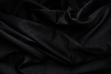 Dark black silky, satin  fabric, wave, draperies. Beautiful textile backdrop. Close-up. Top view 