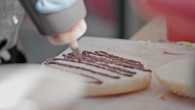 Closeup slow motion shot of chef preparing tasty burgers at outdoor stand. Sauce barbecue, fast food industry and unhealthy lifestyle concept.