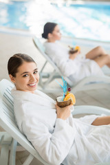 Young woman with tropical drink relaxing on deckchair by swimming-pool