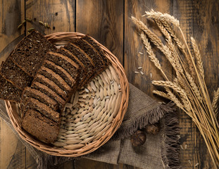 Fototapeta na wymiar Sliced rye bread in a wicker tray and spikelets on wooden surface