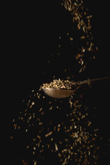 Metal spoon with dry basil, spices falling. Black background. shifted focus.