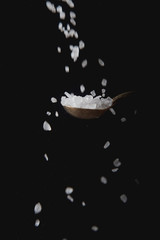 Metal spoon with white salt, spices falling. Black background. shifted focus.