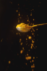 Metal spoon with yellow turmeric. Falling spices. Black background. shifted focus.