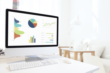 Modern computer with keyboard and mouse on white table showing charts and graph on screen against modern home with chair background , Analysis Business, Statistics Concept.