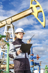 Woman engineer in the oilfield talking on the radio wearing white helmet and work clothes. Toned.