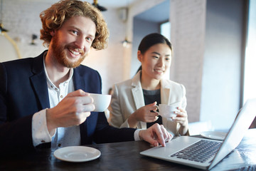 Happy manager with cup of drink and his colleague preparing for business report or project