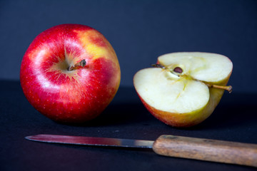 Whole, red, ripe, tasty apple with a knife, half of and apple on black background