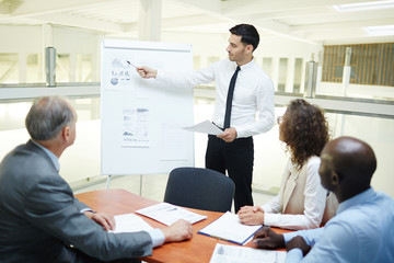 Young confident speaker pointing at financial data on whiteboard and explaining chart