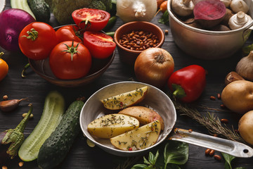 Sliced potato with herbs in the pan on wooden background