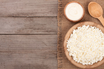 Cottage cheese in a wooden bowl with sour cream on old wooden background with copy space for your text. Top view