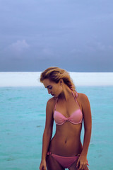 beautiful blonde model posing in sunset sunlight on tropical sea background with white sand.