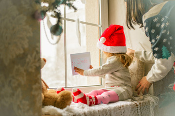 Obraz premium Cute little girl sitting by the window with a letter to Santa Claus