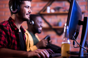 Selective focus of happy young man in headphones is sitting at table with his friend and playing...