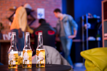 Favorite beverage. Close-up of three bottles of beer are on table. Young stylish guys are resting in background. Copy space in the right side