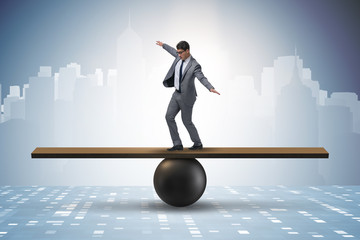 Businessman trying to balance on ball and seesaw