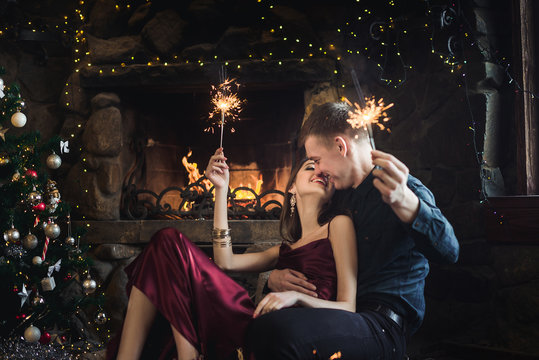 Joyful couple near christmas tree and fireplace with bengal lights selebrate New Year