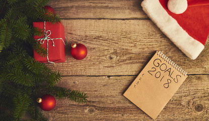 Christmas decorations, notebook with goals for new year and gift boxes over wooden board