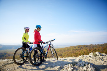 Naklejka na ściany i meble On the mountain. Two cyclist woman enjoying the beautiful scenery while out mountain biking.