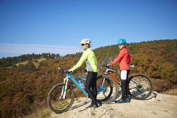 Obraz premium On the mountain. Two cyclist woman enjoying the beautiful scenery while out mountain biking.