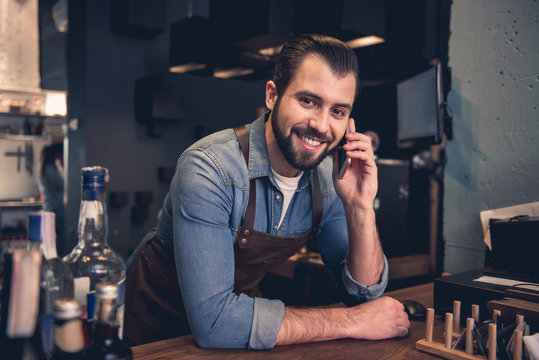 Portrait of happy unshaven worker telling on phone in cafe. He looking at camera. Job concept