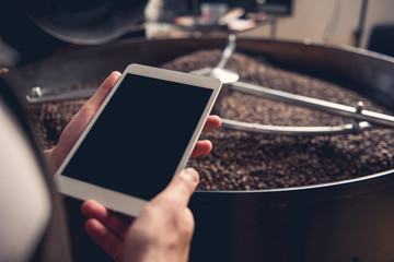 Close up male hand keeping tablet while having job at factory. He situating near technical equipment with coffee grains. Job concept