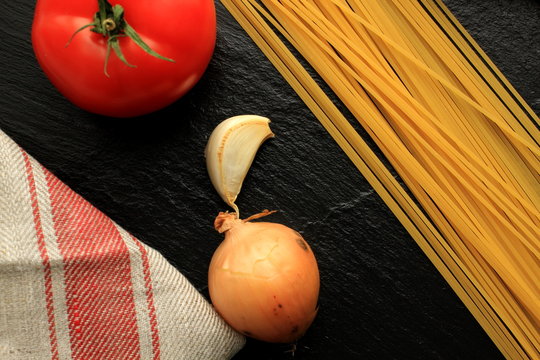 Raw Spaghetti with tomato, onion, garlic and linen kitchen towel on black backgournd