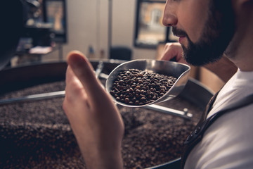 Serene bearded man enjoying burned beans aroma while holding them on spatula. Industry concept. Close up