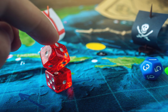 Hand throwing red dice on the world map of the playing field handmade Board games with a pirate ship