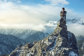 Young man in a sweater with phone in hand on the top of a snowy mountain. Concept availability of mobile connection