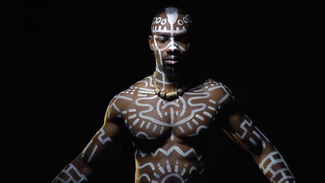 Black Papuan with inflated chest in white patterns dances on a black background, bit slow motion