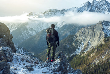 Man hiker with backpack on top of the mountain back, looking at the snow slope. Concept motivation and goal achievement - obrazy, fototapety, plakaty