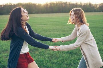 Two cheerful young women dance outdoors. Sunset