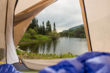 View from tent on a mountain lake. Trips and expeditions in the wild. Concept of camping