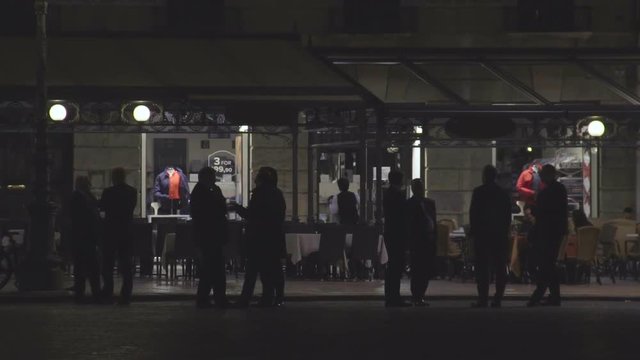 Silhouettes of people talking in front of empty restaurant with tables outside